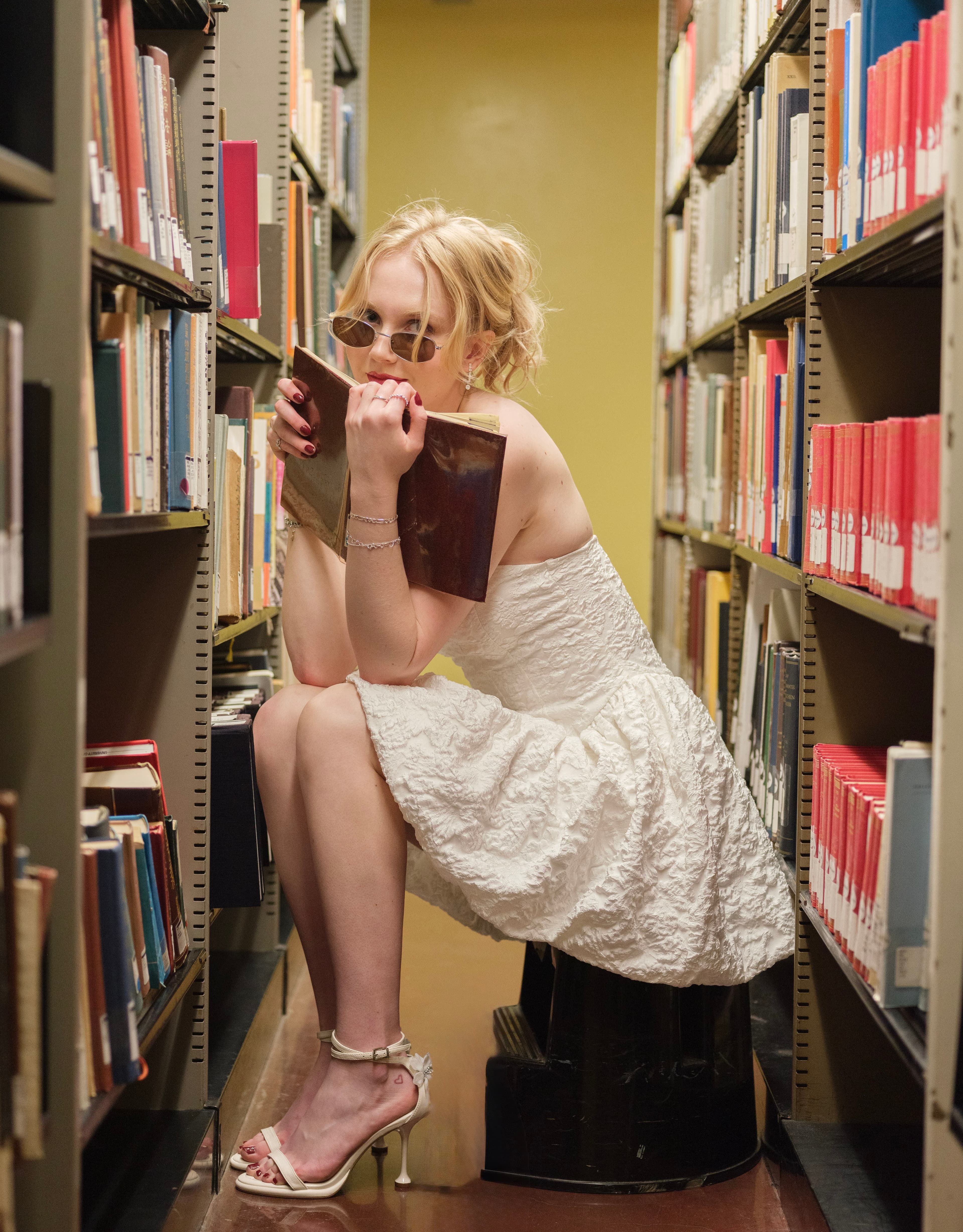 Claire Vivienne seated between library bookshelves, holding a book